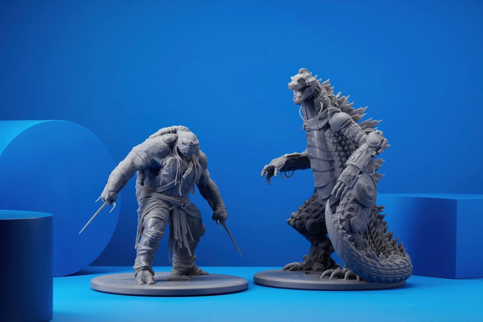 Deux figurines grises imprimées en résine, photographiées sur un fond bleu, avec leurs détails de sculpture et de texture.